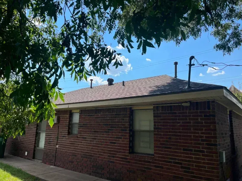 Brick building with a brown roof under a partly cloudy sky. Tree leaves frame the top.