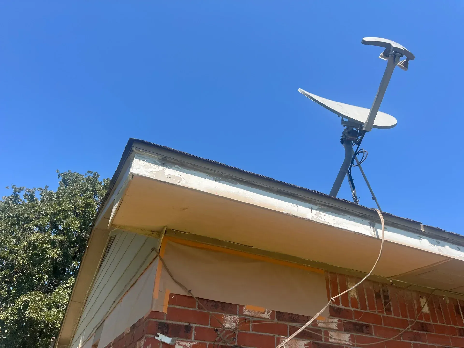 Satellite dish mounted on a brick house roof against a blue sky.