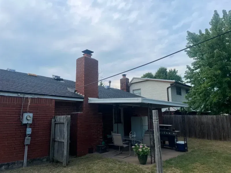 Backyard view with brick house, chimney, patio, and partially cloudy sky.