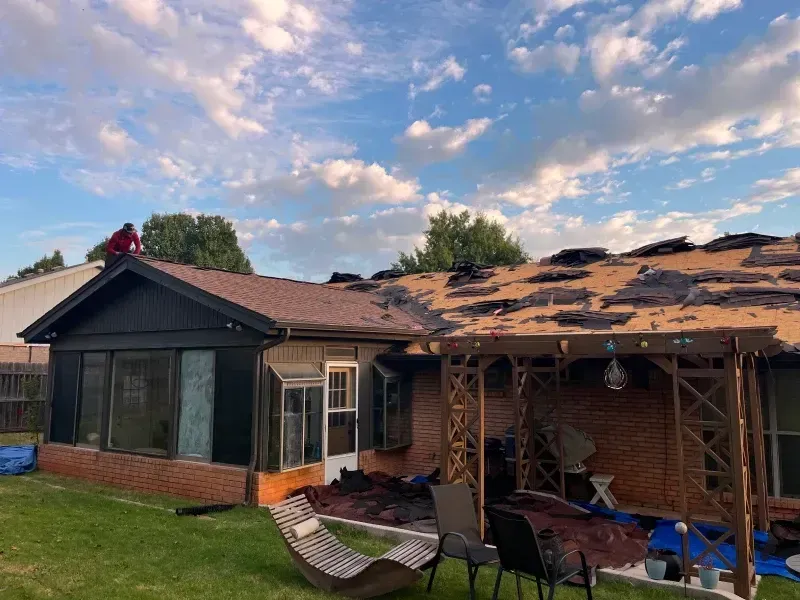 Roof partially torn off a brick house under a cloudy sky. A person works on the roof.