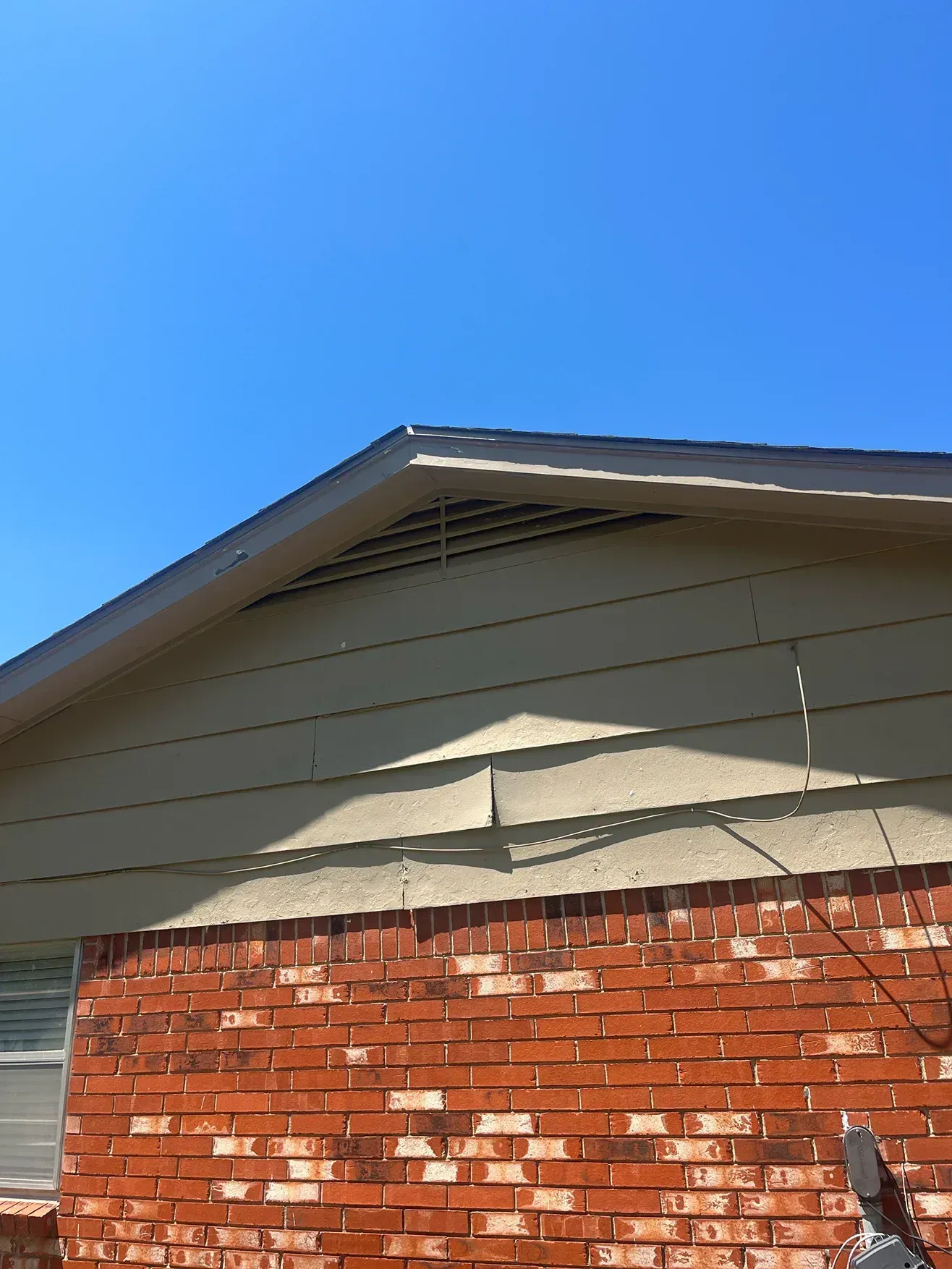 Red brick wall with tan siding and a dark roof against a blue sky.
