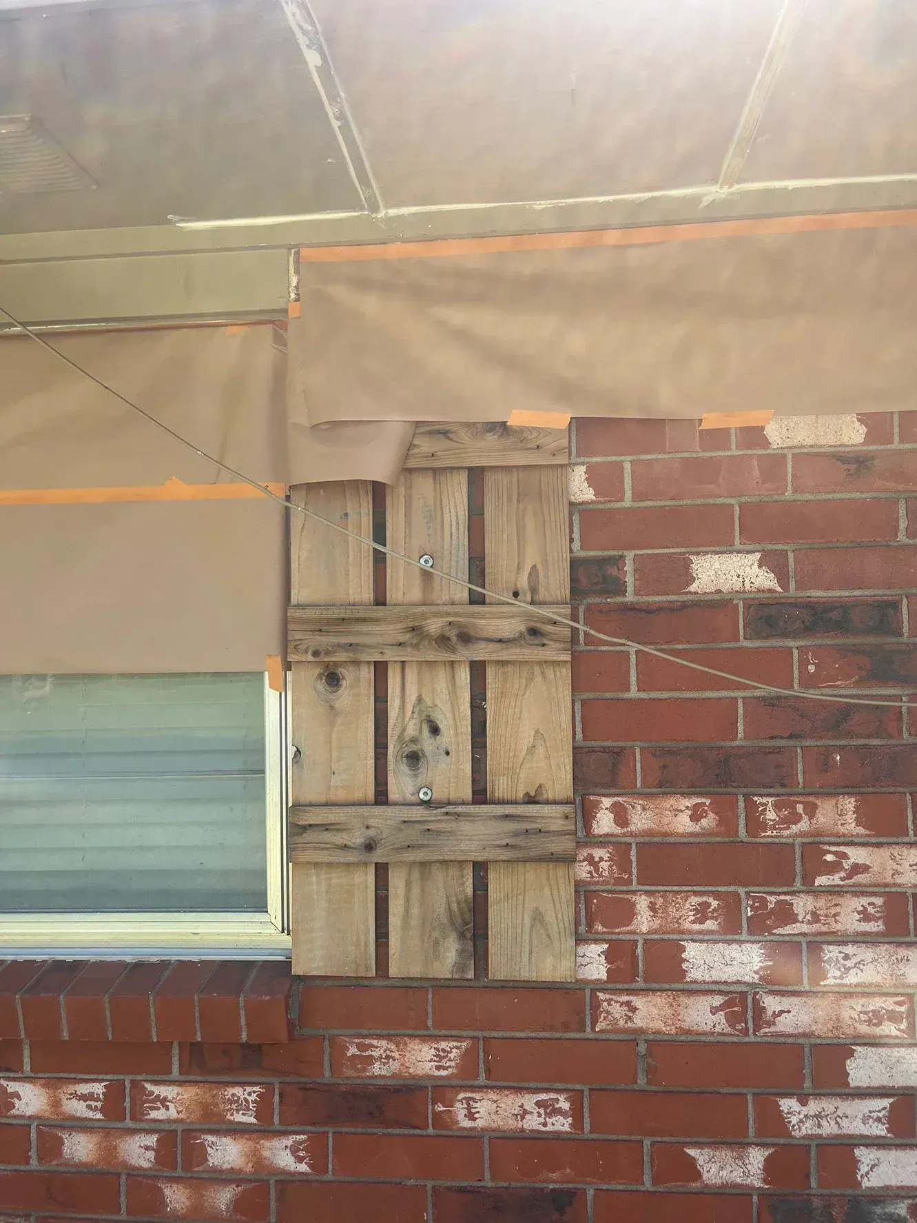 Pallet covering a window on a red brick building, secured with rope.