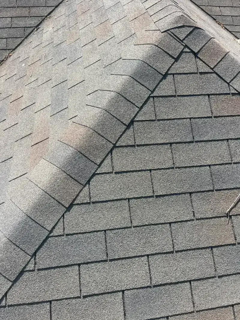 Close-up of a weathered gray and brown shingle roof with a ridge, angled towards the right.