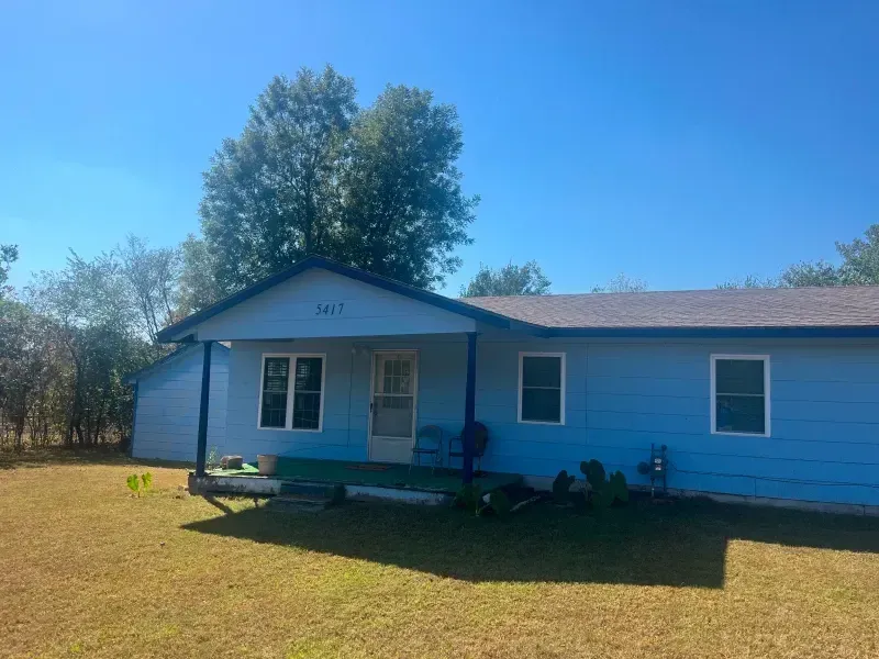 Blue house with a dark blue porch, set on a grassy lawn under a clear blue sky.