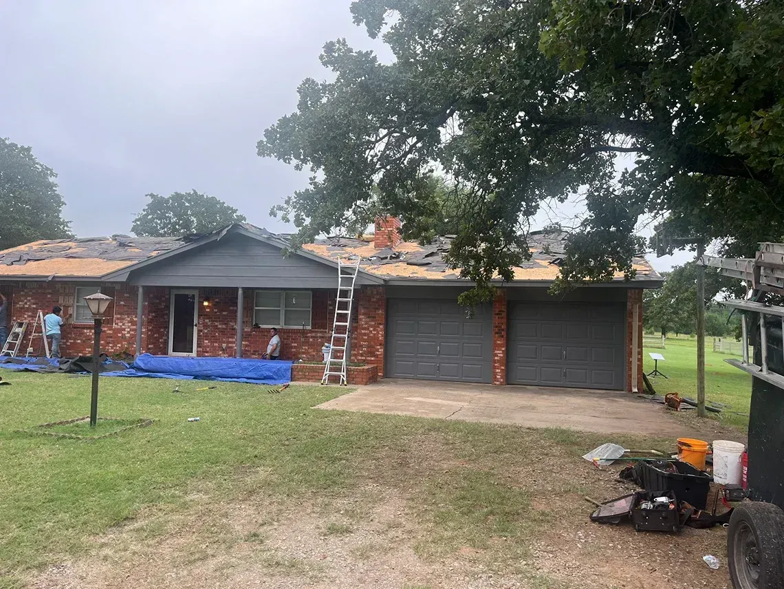 House with roof partially removed, construction underway. Brick exterior, two-car garage, ladder against the roof.