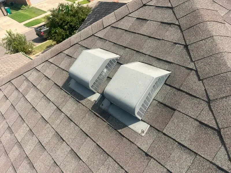 Two gray roof vents on a brown shingle roof, angled view.