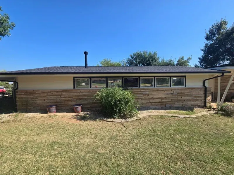 Side view of a ranch-style house with a brick facade and dark roof. The windows are black-framed.
