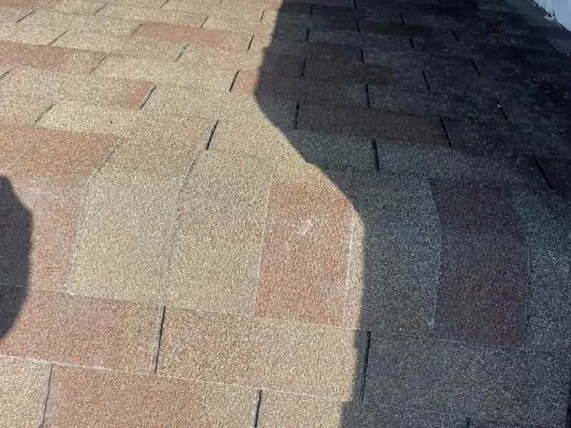 Close-up of asphalt shingle roof in various shades of brown, with a shadow across the right side.
