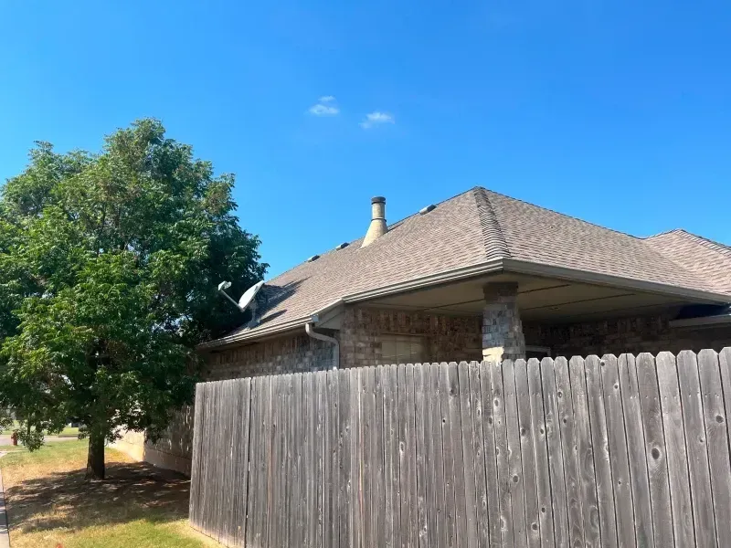 A house with a brown roof and a wooden fence under a clear blue sky.