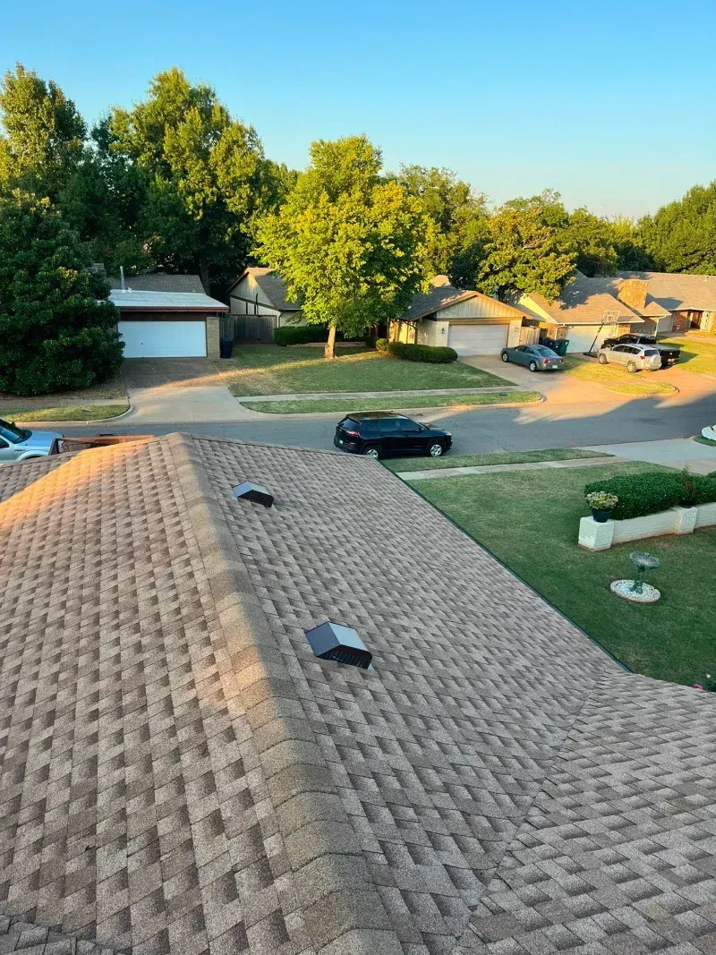 View of residential rooftops and neighborhood with cars and trees.