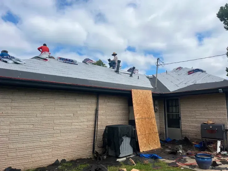 Roofers installing new shingles on a house roof under a cloudy sky.
