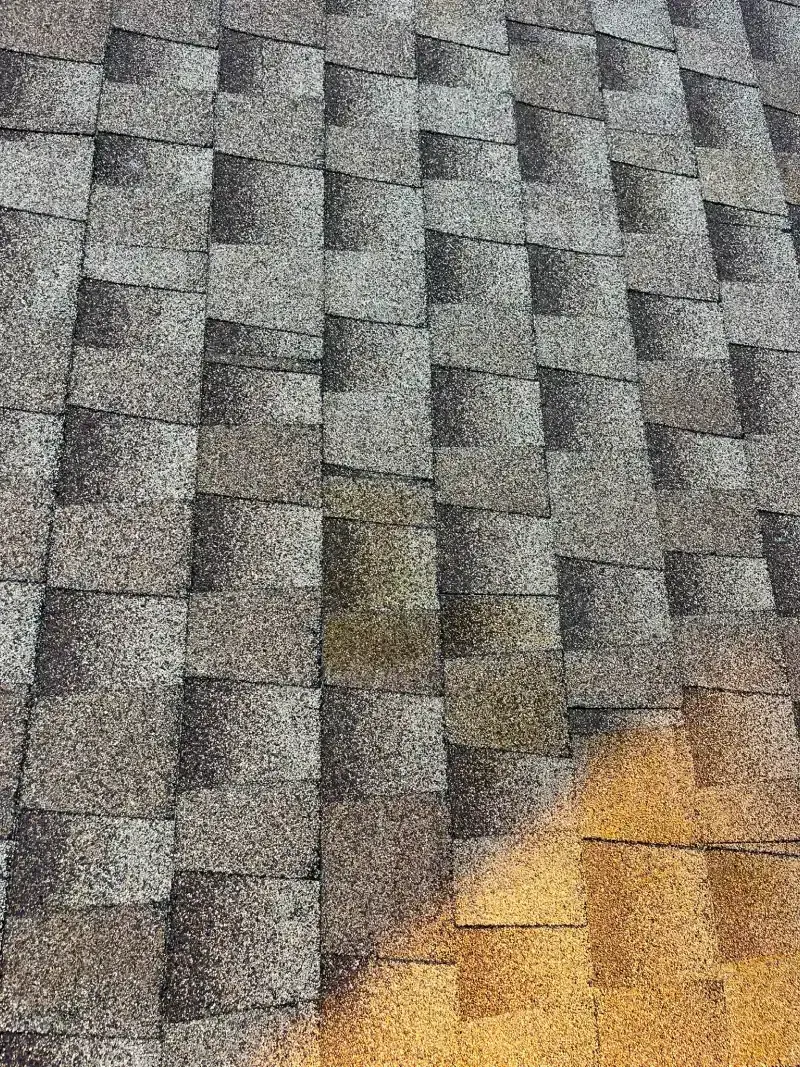 Close-up view of a shingle roof with dark gray and weathered shingles. Some shingles show discoloration.