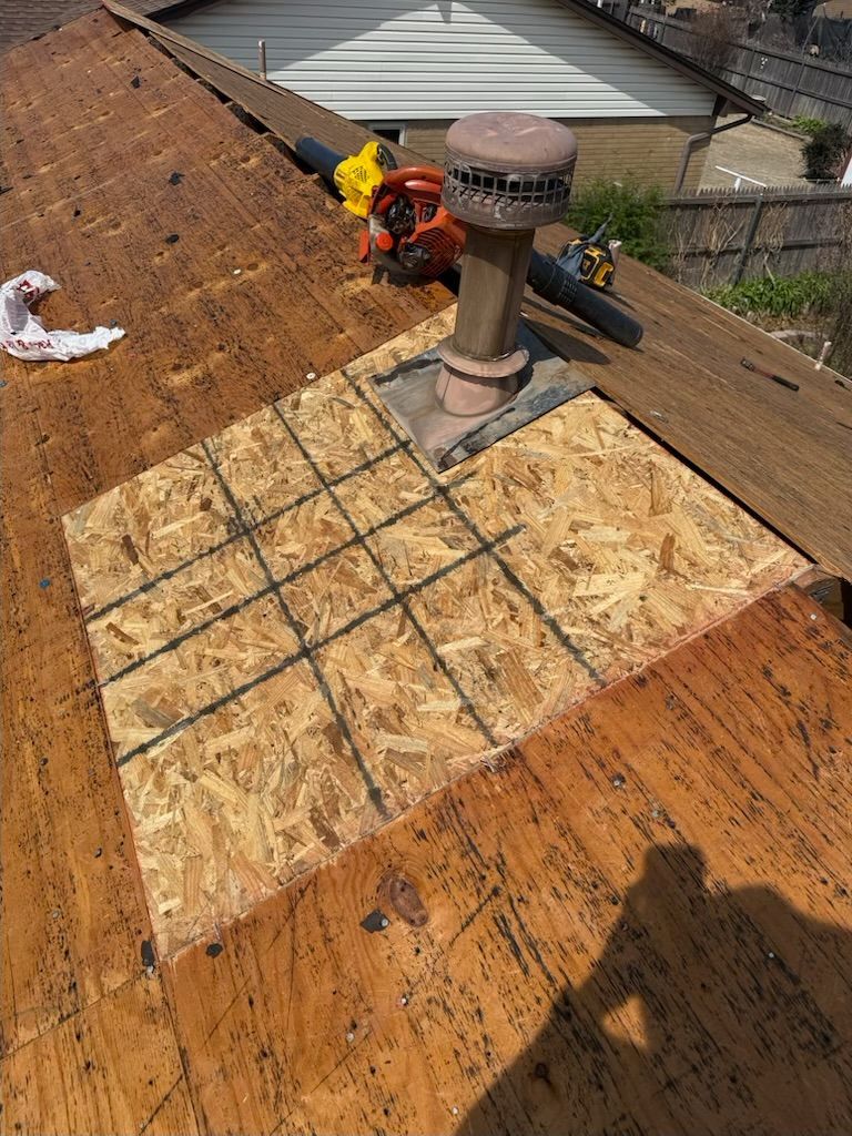 Roof repair with plywood patch around a chimney on a brown shingled roof, tools nearby.