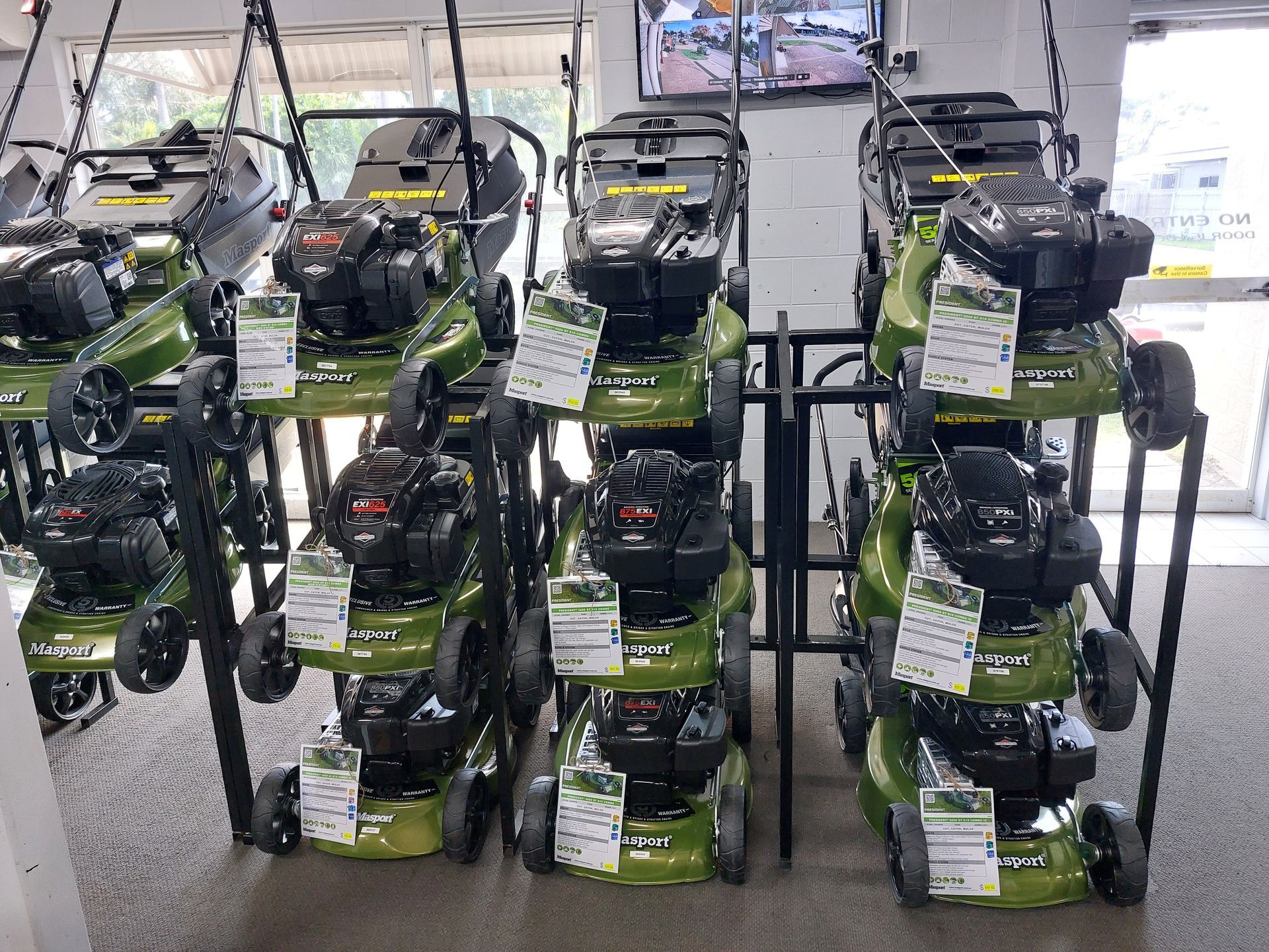 Row of Green-Black Lawn Mowers Displayed on Metal Shelving — Professional Small Engines in Aitkenvale, QLD