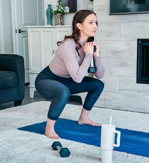 A woman is squatting on a yoga mat while holding a dumbbell. Forever Fit - Personalised Workouts and Nutrition