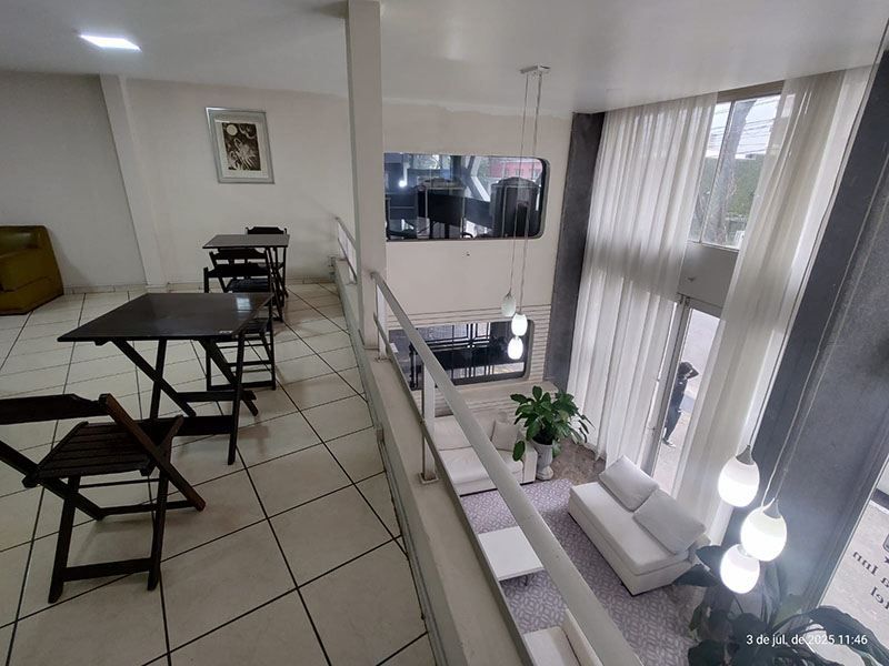 Vista elevada do interior de um edifício moderno, com um mezanino com mesas e uma sala de estar no piso inferior.