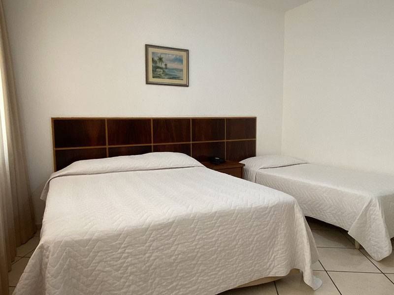 Um quarto de hotel com uma cama de casal e uma cama de solteiro lado a lado, com lençóis brancos e cabeceira revestida de madeira.