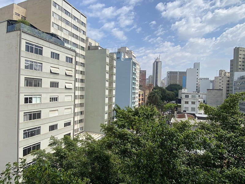 Vista de vários prédios altos de apartamentos e escritórios sob um céu claro, parcialmente nublado, emoldurados por árvores verdes.