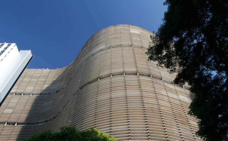 Vista de baixo para cima da fachada ondulada e com nervuras de concreto do Edifício Copan em São Paulo, contra um céu azul brilhante.