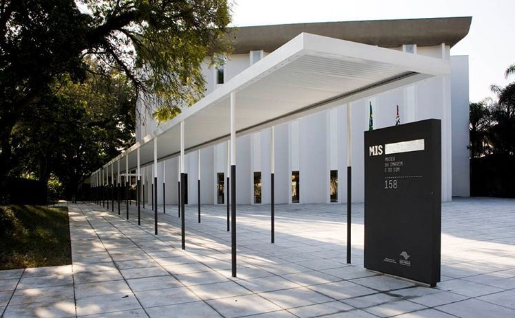 Uma passarela coberta de branco leva à entrada do moderno edifício branco do MASP, com uma placa informativa preta na frente.