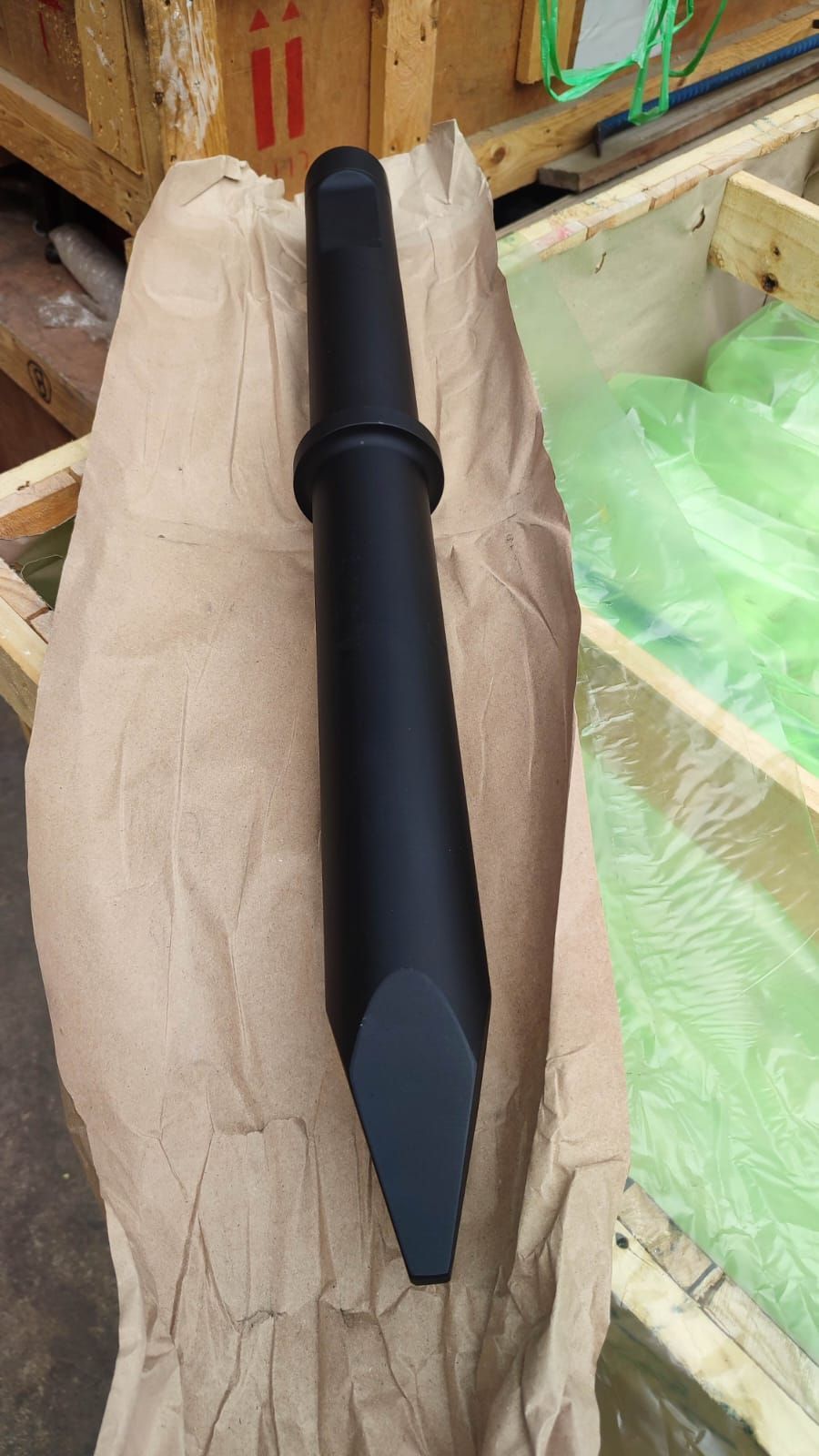 Herramienta de cincel negro que reposa sobre papel marrón, dentro de una caja de madera.