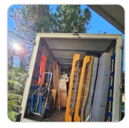 Open moving truck packed with wooden boards, ladders, and tools, viewed from the rear under a blue sky