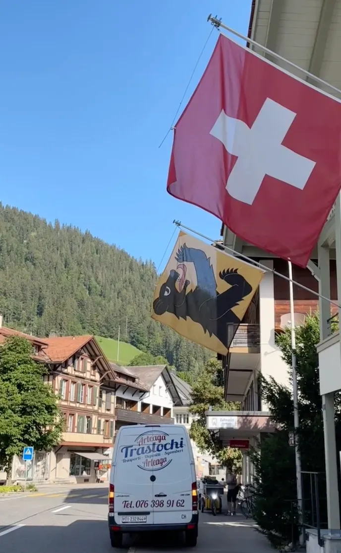 a white van Arteaga Traslochi is parked on the side of the road next to a swiss flag .