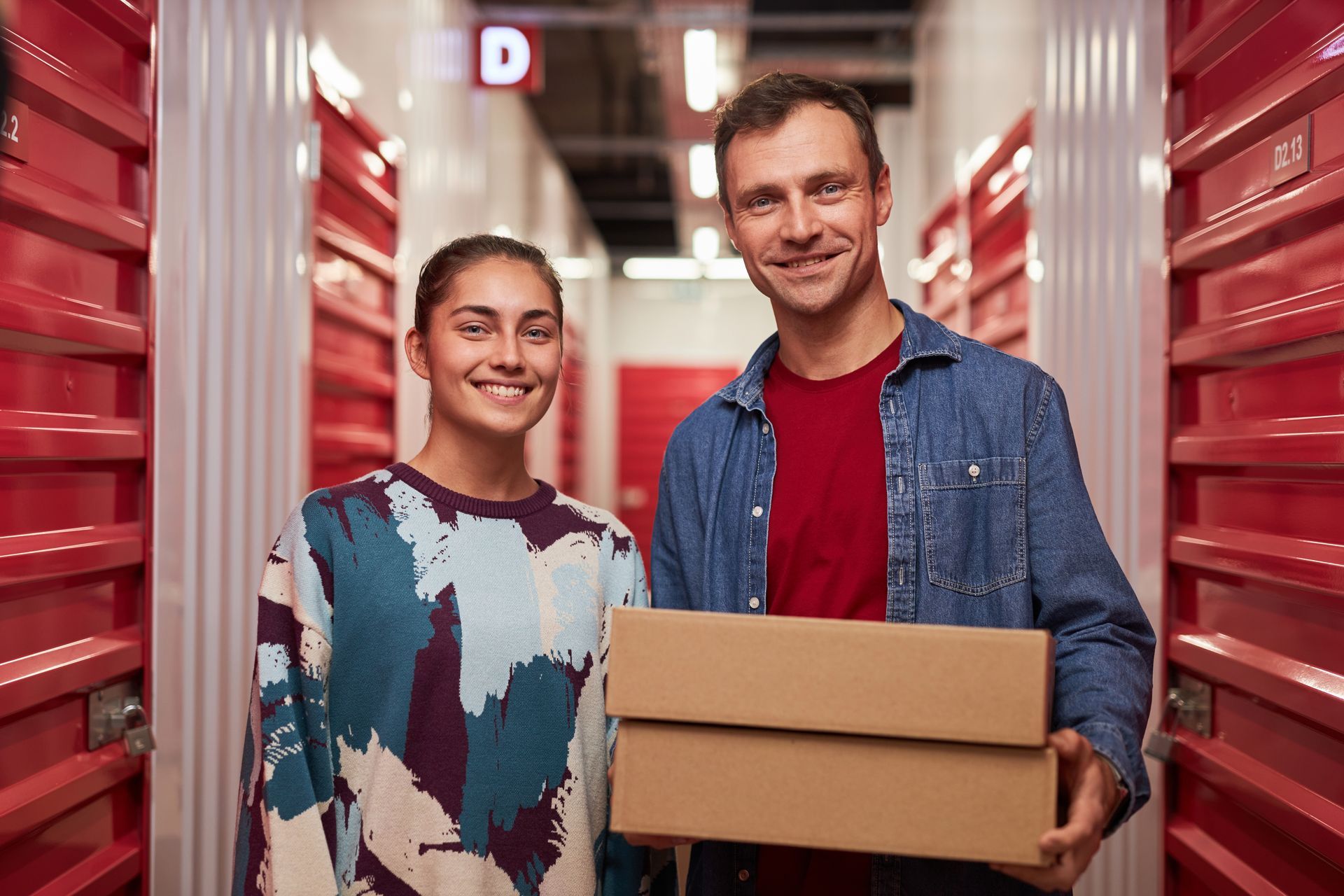 A man and a woman are holding a cardboard box in a storage room.
