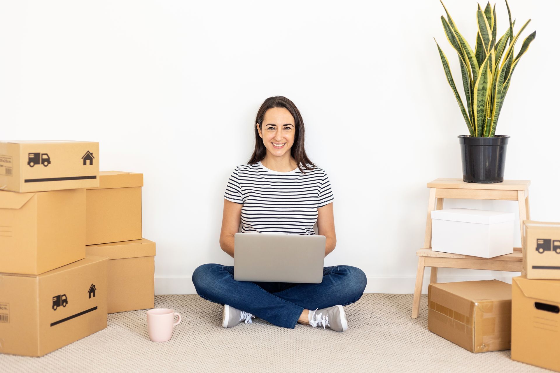 compila la tua richiesta di preventivo per un Trasloco professionale con Arteaga Traslochi una donna è seduta sul pavimento con in mano un computer portatile .