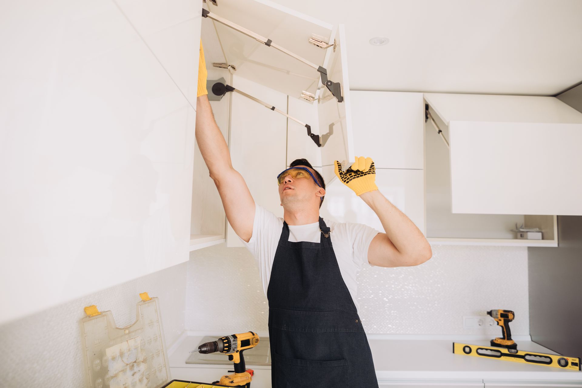 A man in an apron is working on a kitchen cabinet.