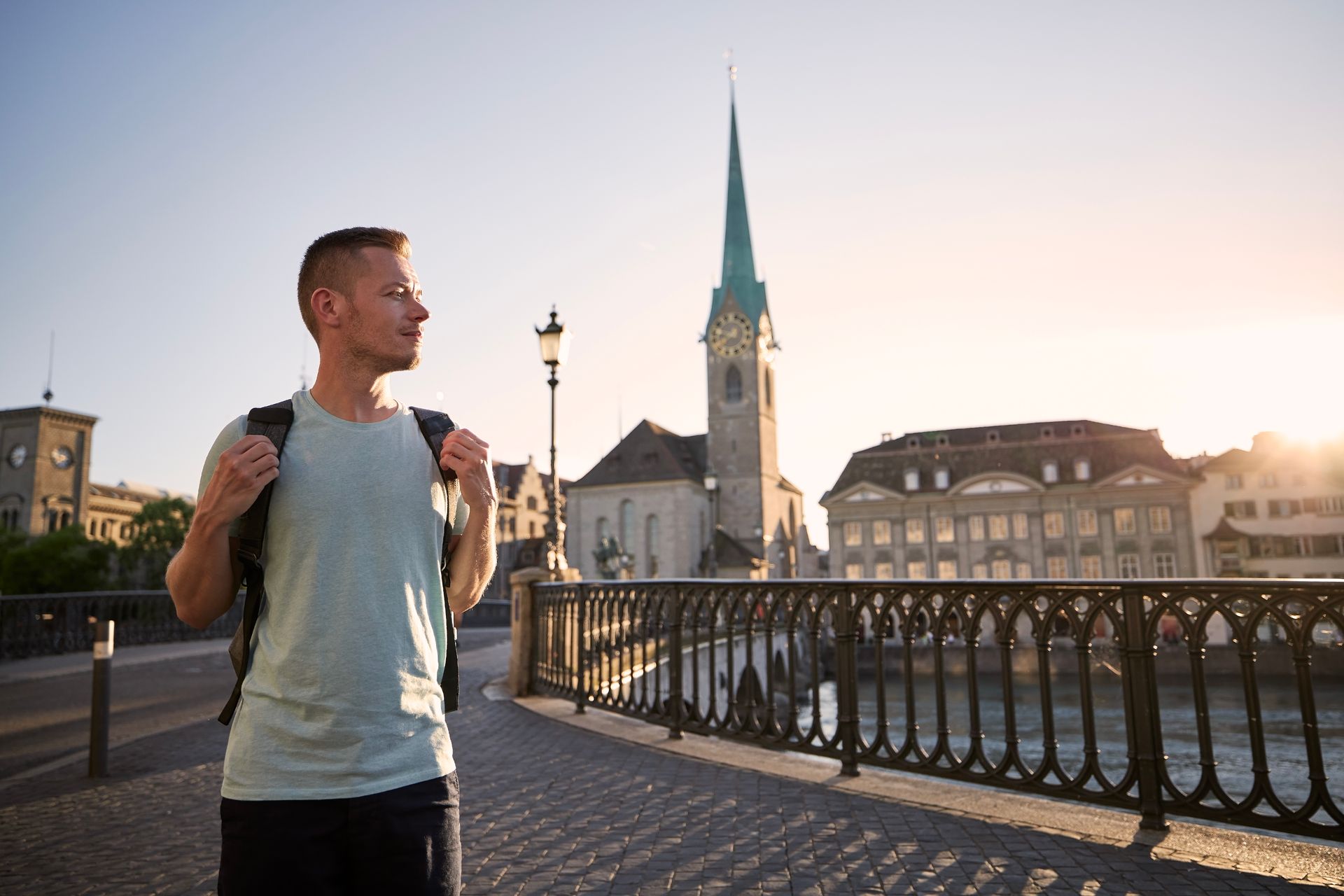 A man with a backpack is standing on a bridge over a river.