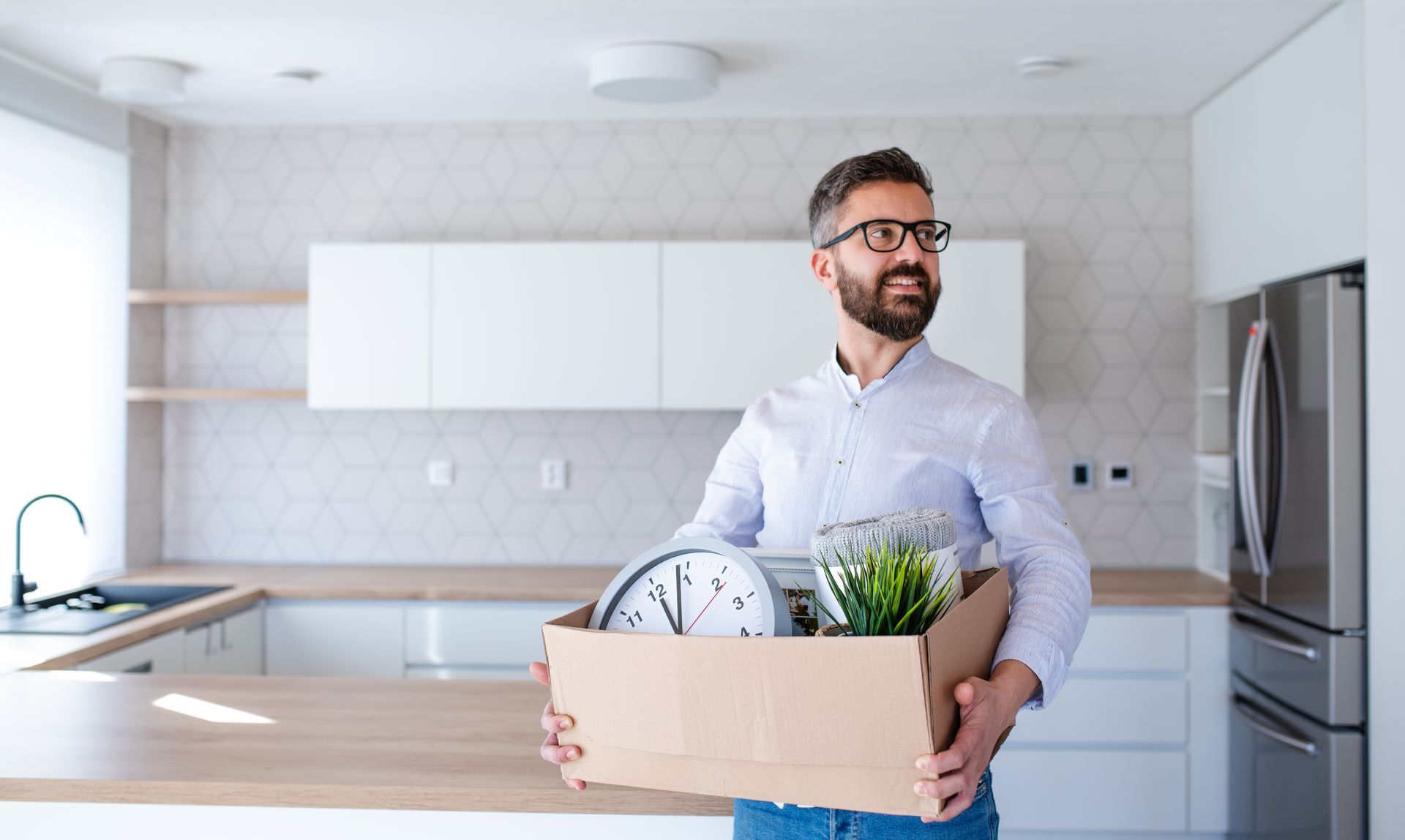 A man is holding a box with a clock in it in a kitchen.