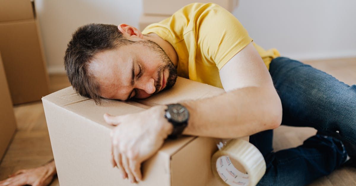A man is laying on the floor sleeping on a cardboard box.