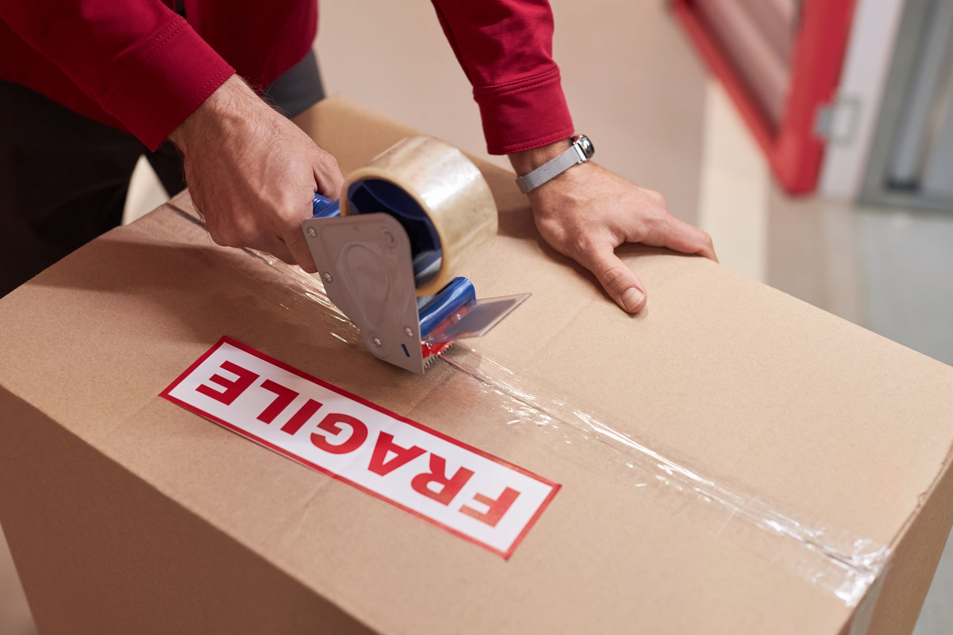 A man is taping a cardboard box with fragile tape.