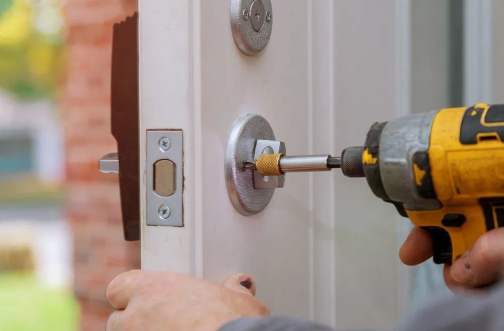Person Using a Yellow Power Drill to Install a Door Lock on a White Door — CTS Locksmiths in Maroochydore, QLD