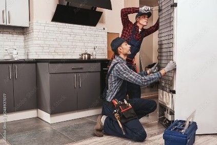 Two technicians repairing a refrigerator in a home kitchen.