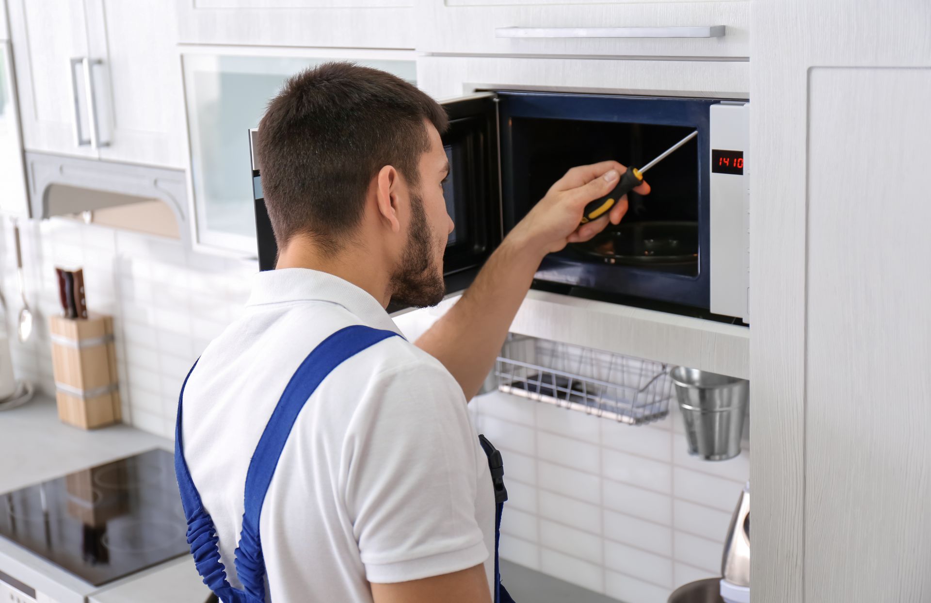 An expert appliance repair technician fixing a microwave oven in a modern kitchen. An expert appliance repair technician fixing a microwave oven in a modern kitchen.