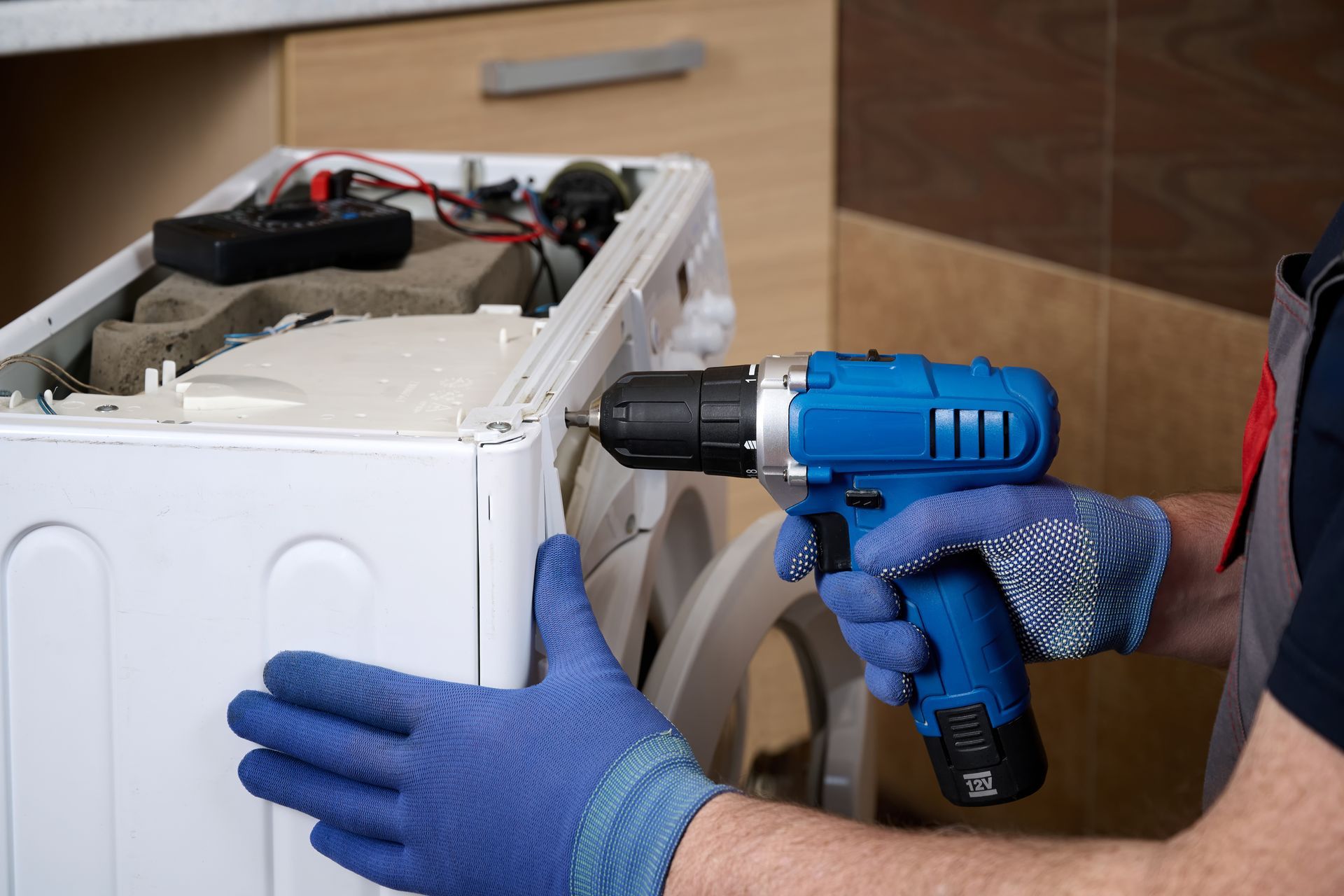 Technician performing home appliance repair on a kitchen refrigerator.