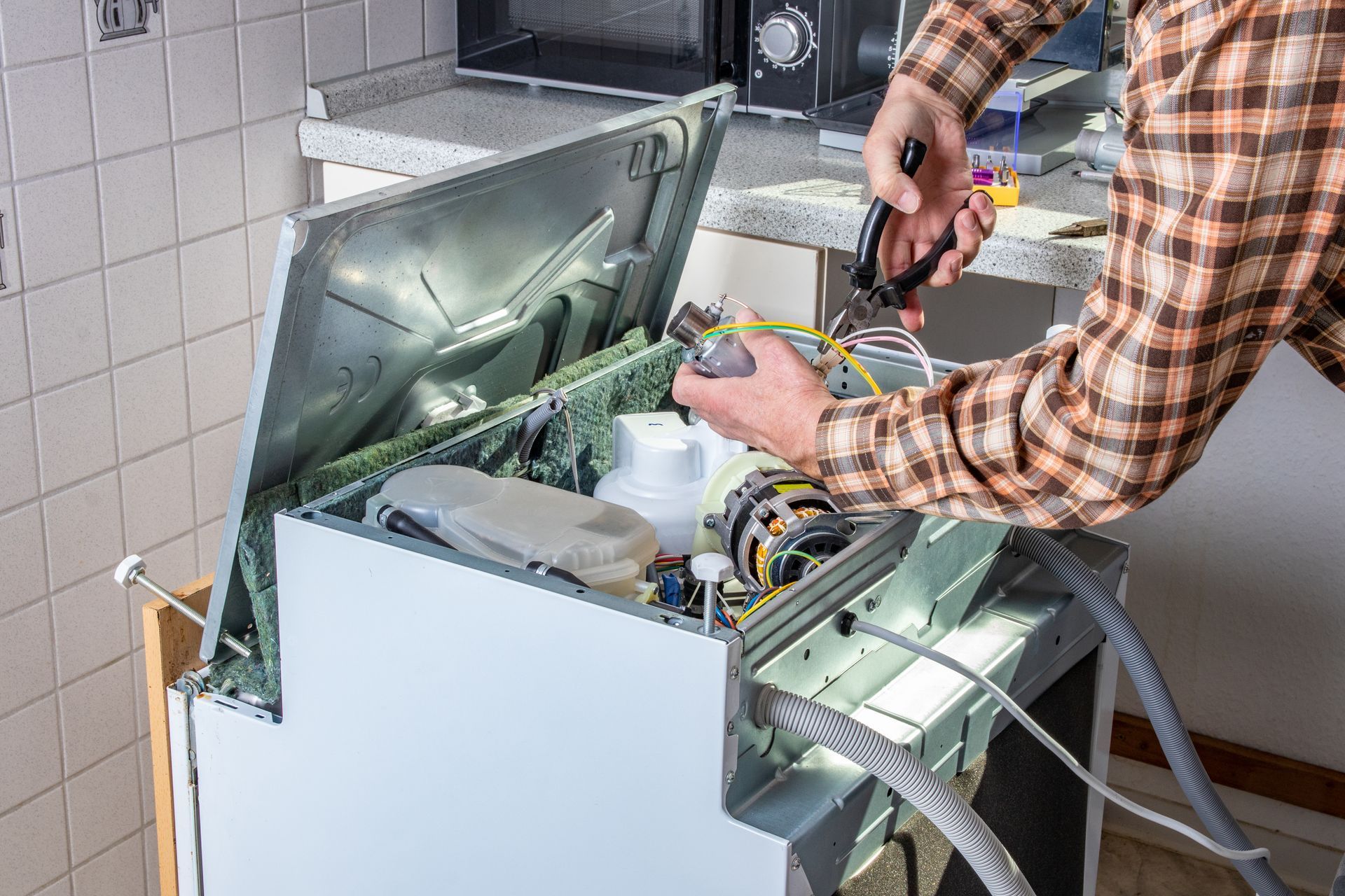 Home appliance repair technician servicing a dishwasher in a kitchen.