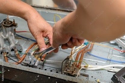 Technician using a wrench to repair internal appliance wiring and components.