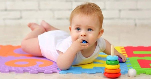 Baby on stomach on mat with toys. The baby is holding a blue toy in its mouth