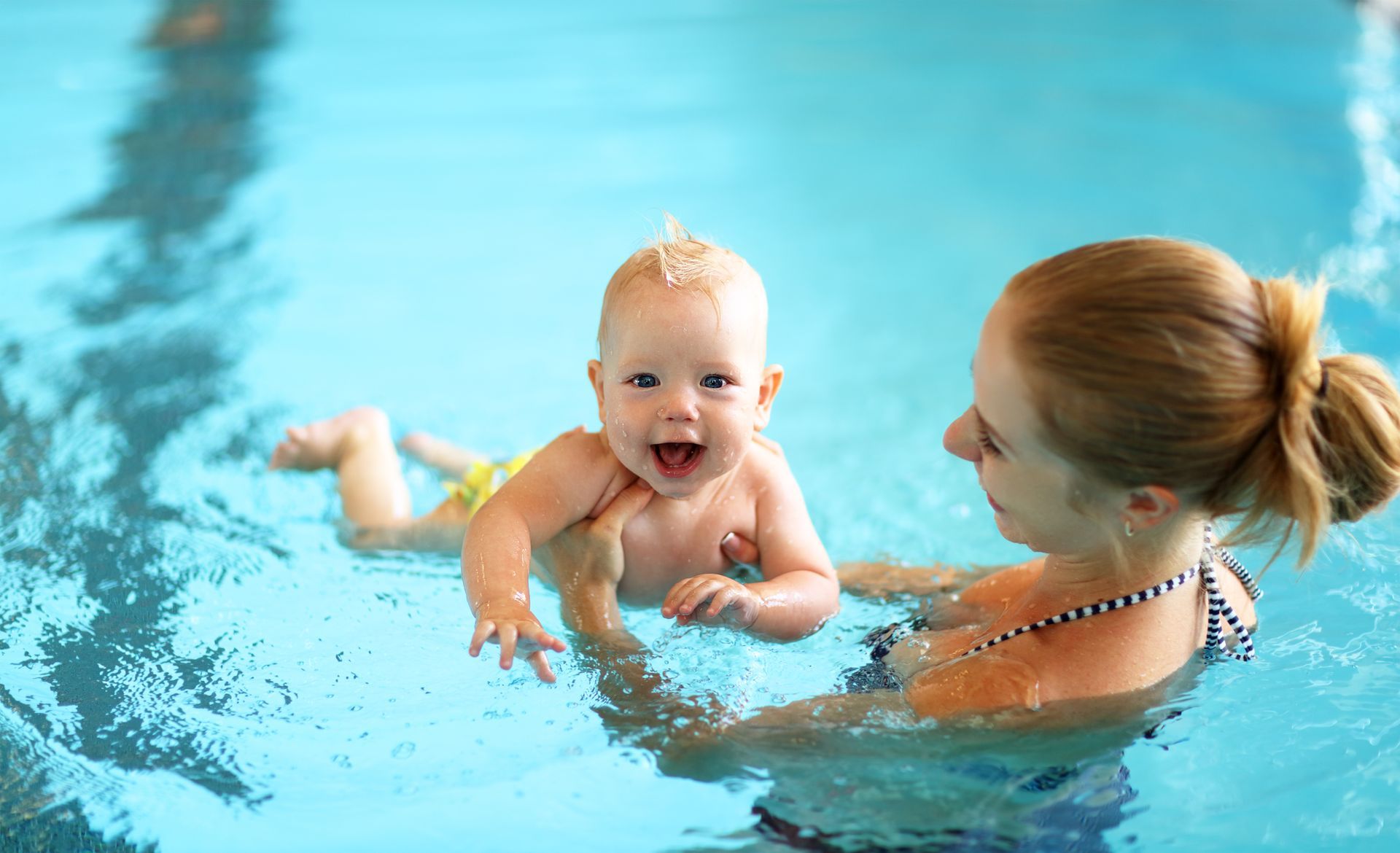 Mother holding her baby in the water during a swimming lesson, focusing on water safety 