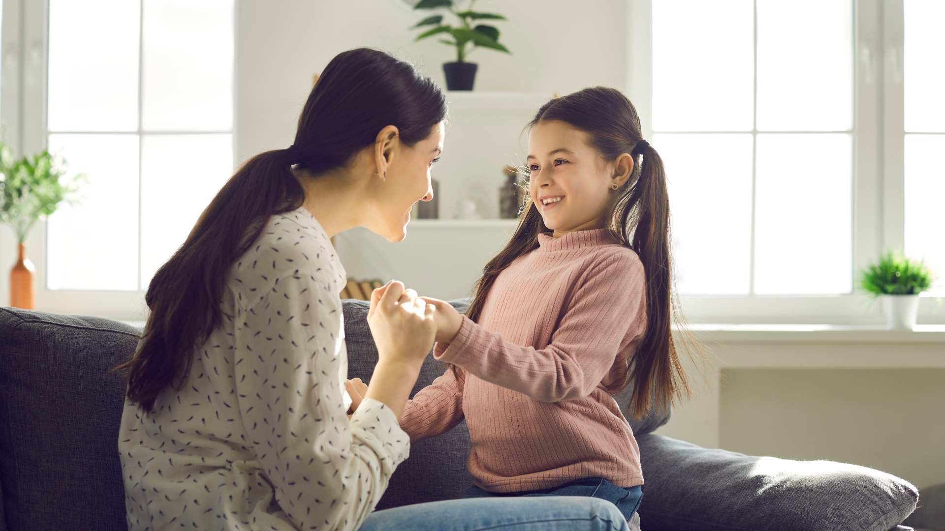 A woman and a little girl are sitting on a couch playing with each other.