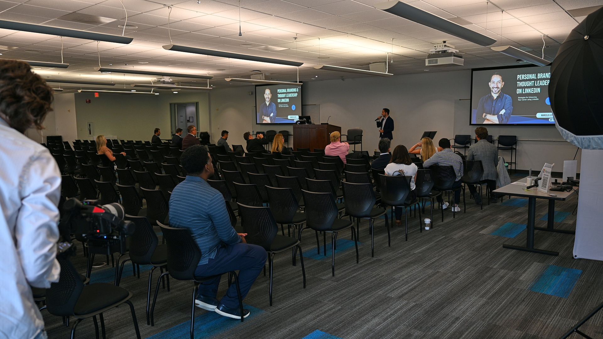 A group of people are sitting in a lecture hall watching a presentation.