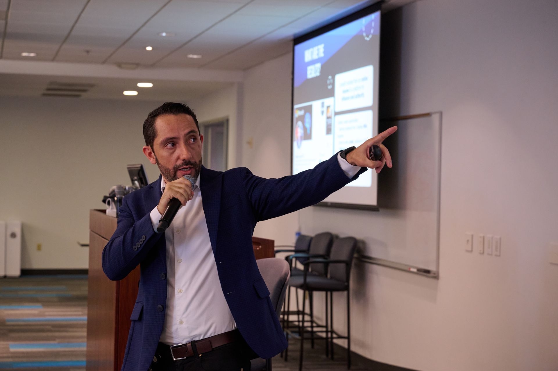 A man in a suit is giving a presentation in front of a projector screen.