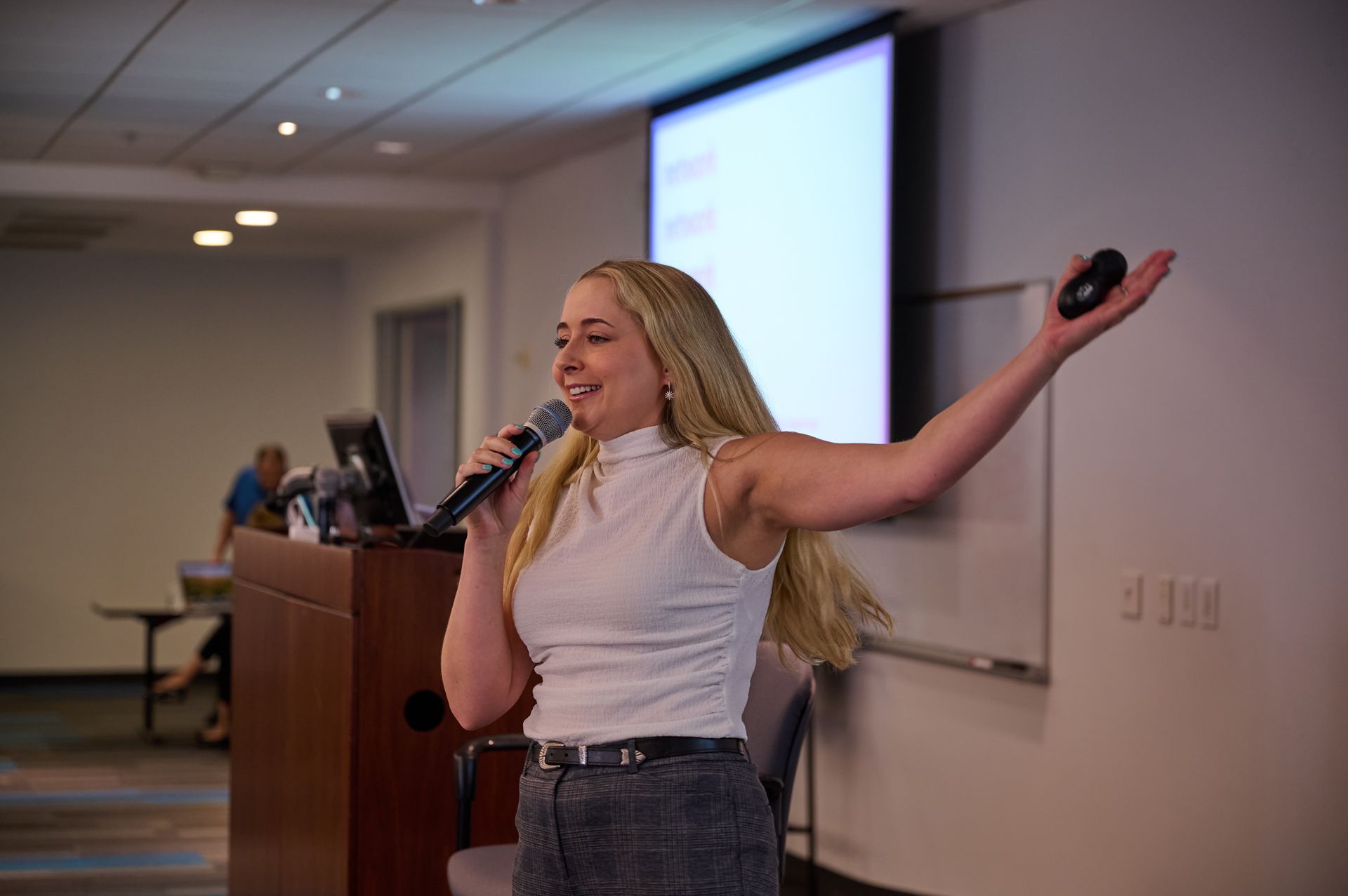 A woman is giving a presentation in a classroom while holding a microphone.