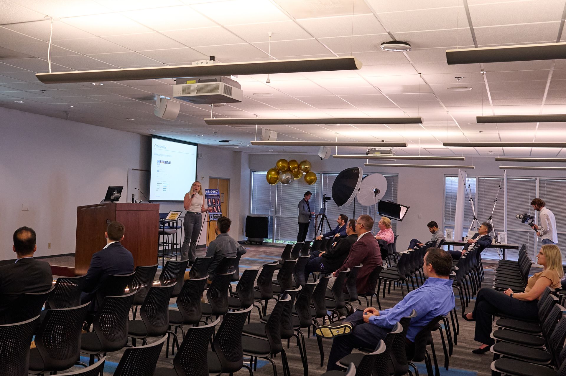 A group of people are sitting in chairs in a large room watching a presentation.