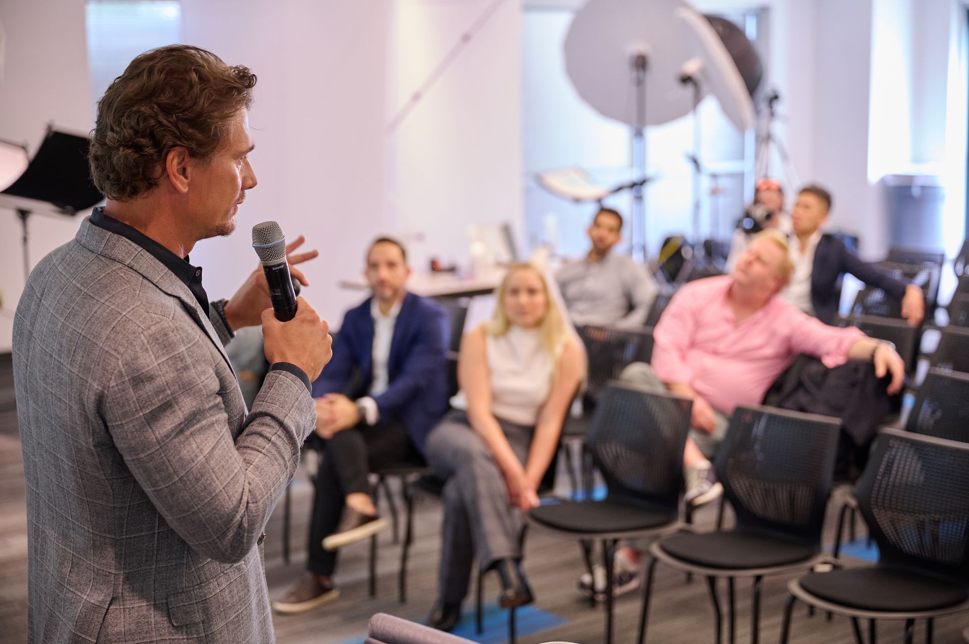 A man is holding a microphone in front of a group of people sitting in chairs.