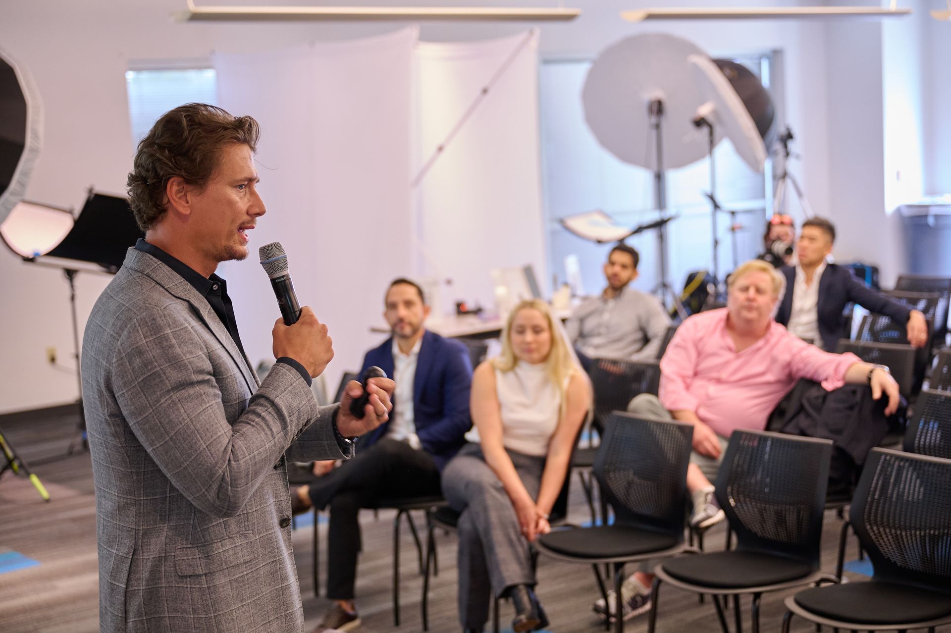 A man is holding a microphone in front of a group of people sitting in chairs.
