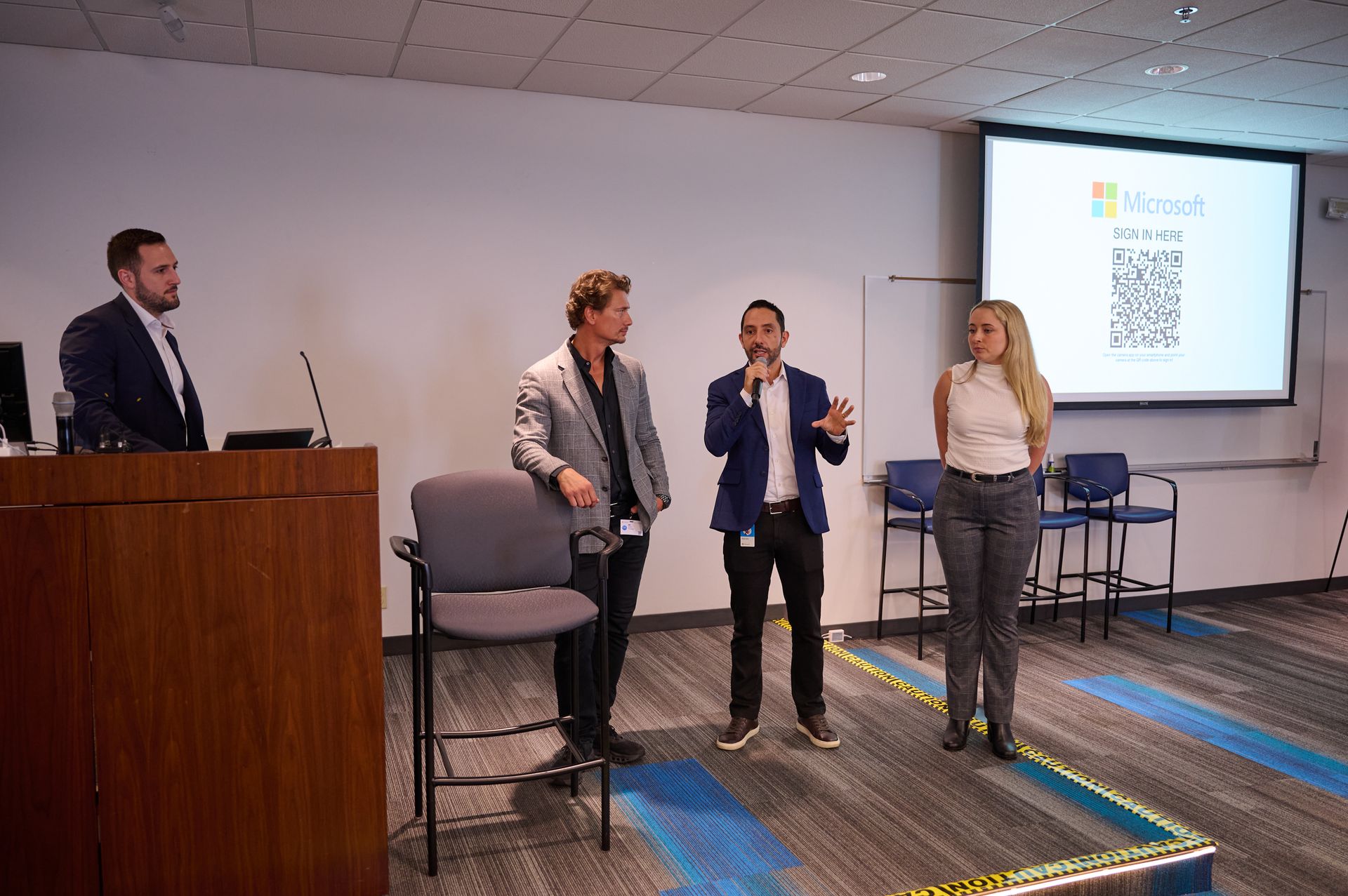 A group of people are standing in front of a projector screen in a conference room.